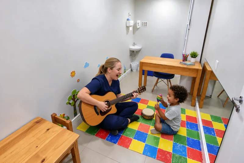 Musicoterapeuta toca violão enquanto criança acompanha com maraca