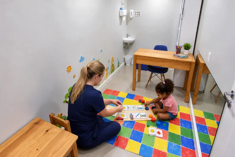 Terapeuta organiza rotina visual com pictogramas ao lado de criança em sessão de ABA