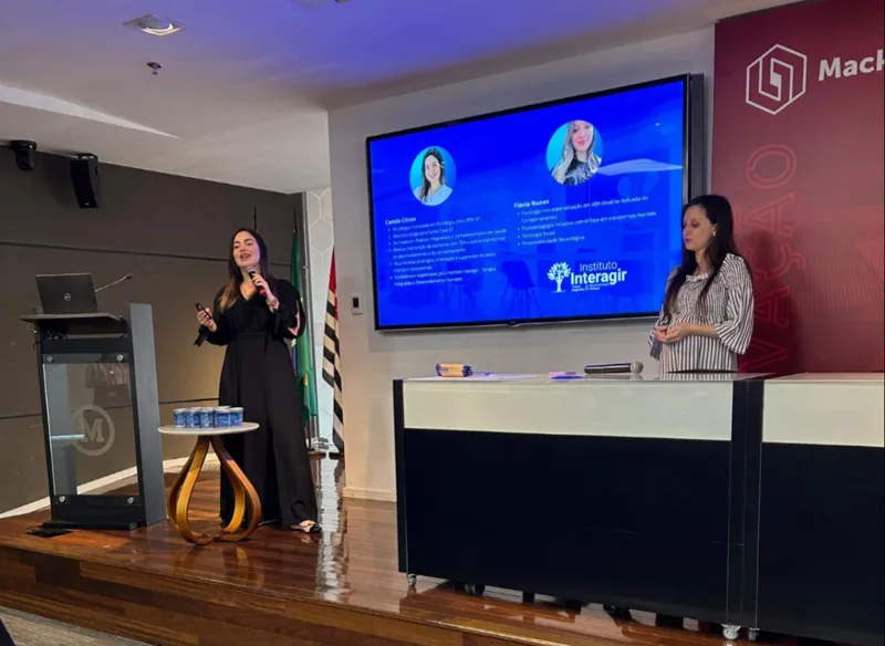 Profissionais do Instituto Interagir apresentando uma palestra em universidade, com a apresentação da equipe no telão