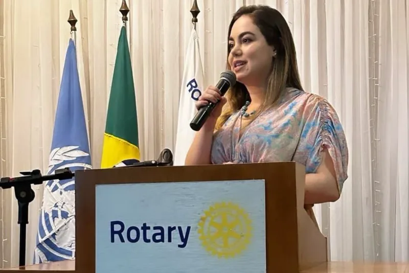 Palestrante do Instituto ao púlpito em evento do Rotary, com bandeiras ao fundo
