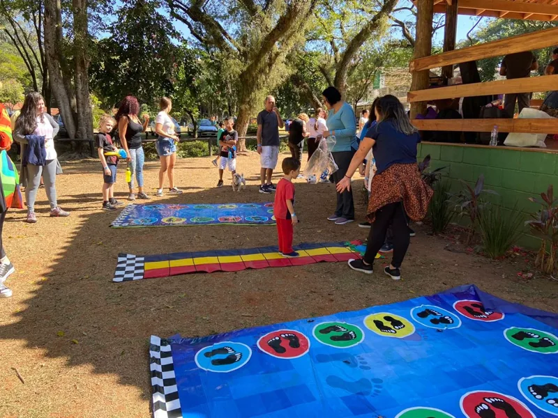 Jogos gigantes de tabuleiro estendidos no gramado do parque, com crianças e adultos participando